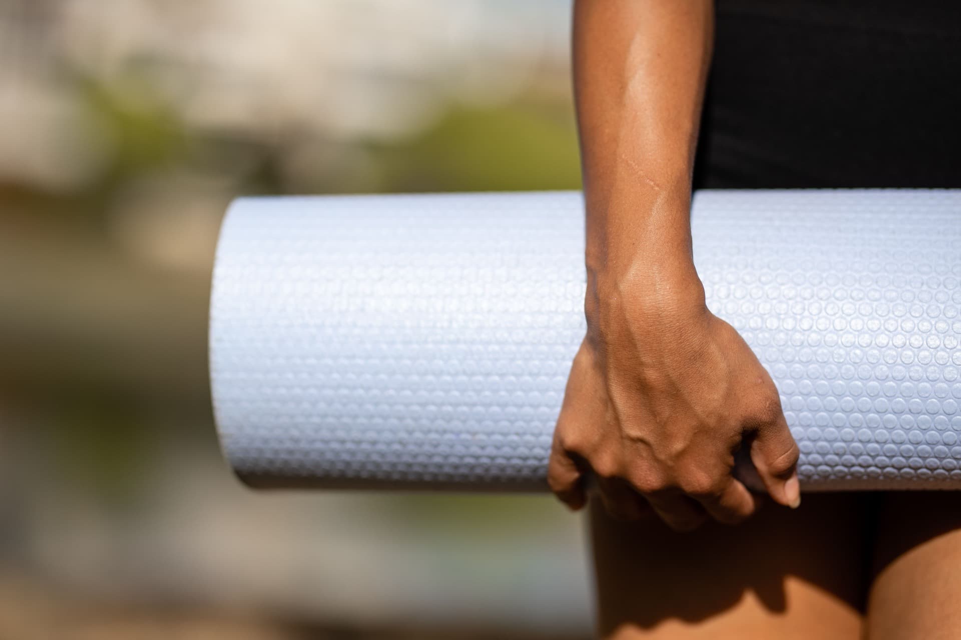 A hand carrying a rolled yoga mat, backlit